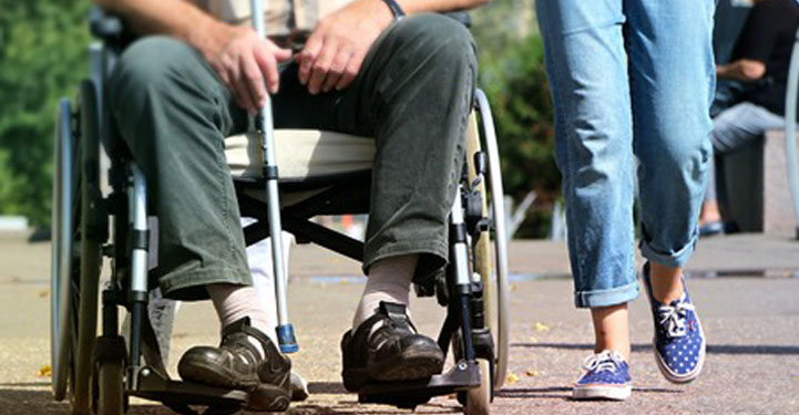 Un homme en fauteuil roulant accompagné par une jeune aide soignante