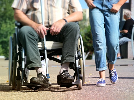 Un homme en fauteuil roulant accompagnée par une jeune assistante